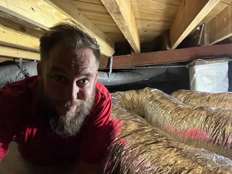 A team member under a house inspecting air ducts